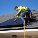 A worker installing solar panels on a building roof using safety gear