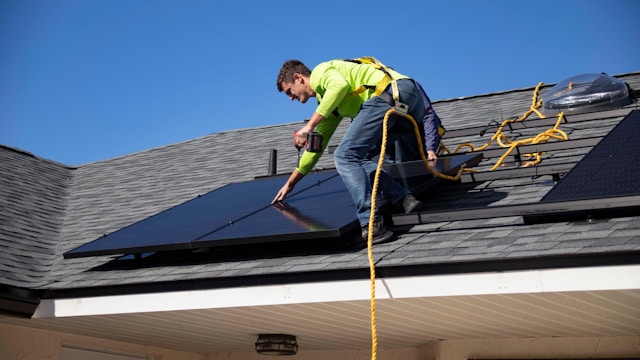 A worker installing solar panels on a building roof using safety gear