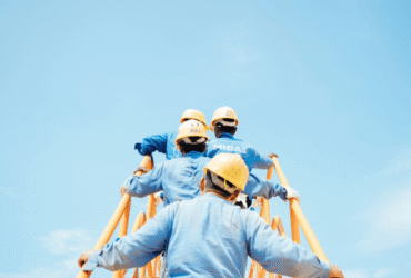 Construction workers in safety gear climbing scaffolding under a clear blue sky, symbolizing teamwork and improved workplace conditions.