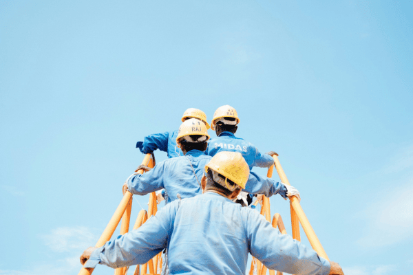 Construction workers in safety gear climbing scaffolding under a clear blue sky, symbolizing teamwork and improved workplace conditions.