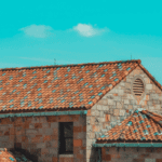 Close-up view of a house with red tile roofing under a bright blue sky, representing quality roof installation and contractor expertise.