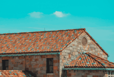 Close-up view of a house with red tile roofing under a bright blue sky, representing quality roof installation and contractor expertise.