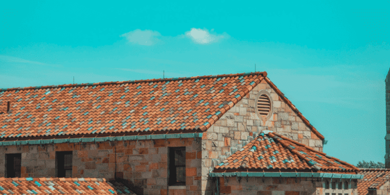 Close-up view of a house with red tile roofing under a bright blue sky, representing quality roof installation and contractor expertise.