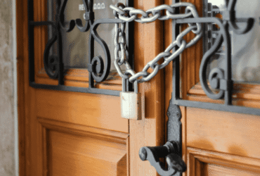 Close-up of a wooden door secured with a chain and padlock, representing enhanced home security.