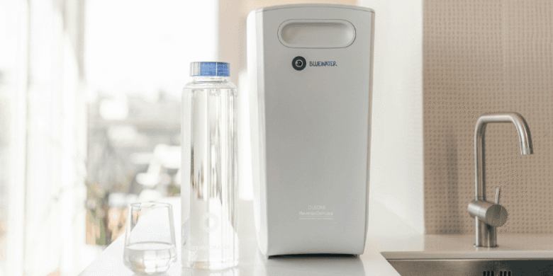 Compact home water filtration system placed on a kitchen counter beside a sink and reusable bottle, representing cleaner water and reduced household waste.