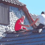Two workers inspecting and repairing a residential roof, highlighting how routine roof inspections can help prevent costly structural damage.