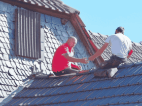 Two workers inspecting and repairing a residential roof, highlighting how routine roof inspections can help prevent costly structural damage.
