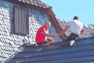 Two workers inspecting and repairing a residential roof, highlighting how routine roof inspections can help prevent costly structural damage.