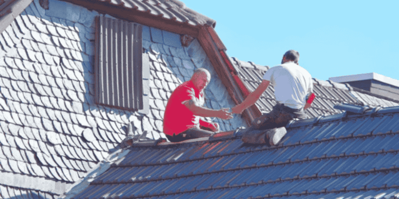 Two workers inspecting and repairing a residential roof, highlighting how routine roof inspections can help prevent costly structural damage.